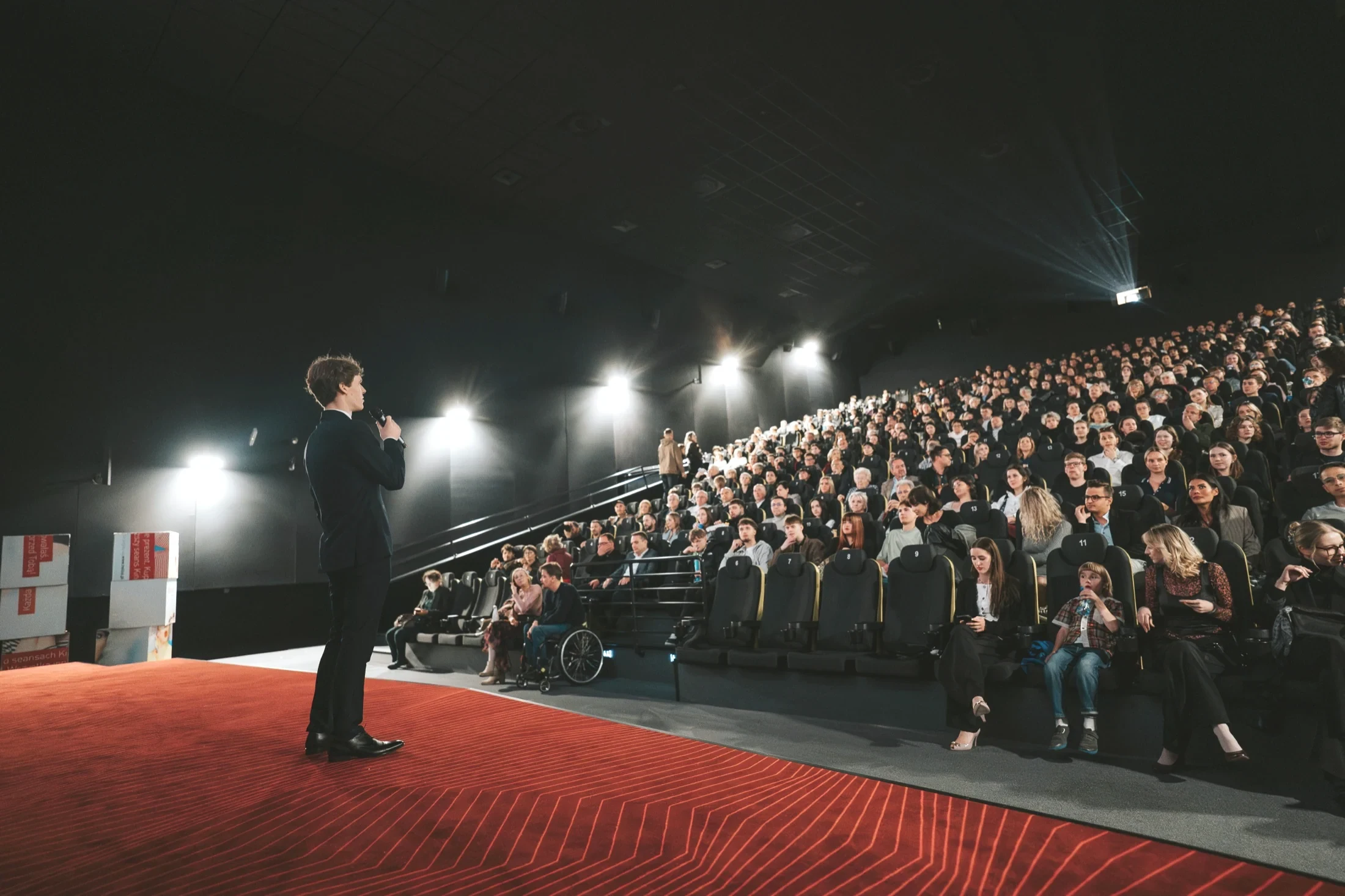A packed cinema house on the Tena lavitra screening tour, the host alone on the red-lit stage before the audience.