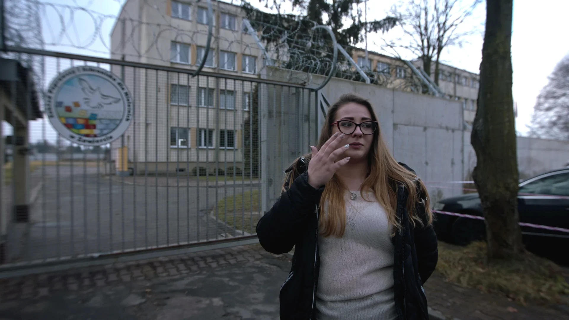 A young woman outside the razor-wire gate of a juvenile facility, from the documentary Młodość, prawo i odpowiedzialność.